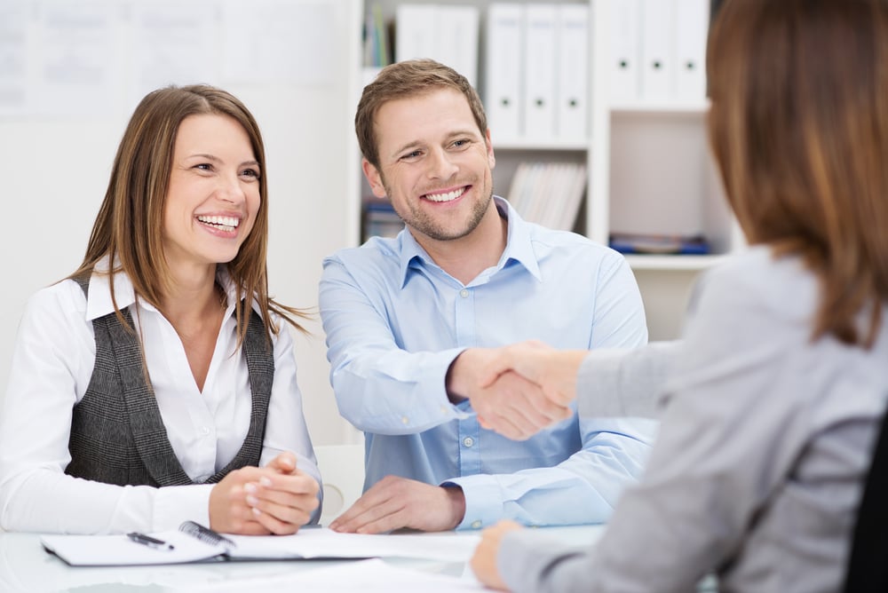 A young couple shaking hands with an insurance agent over a desk.